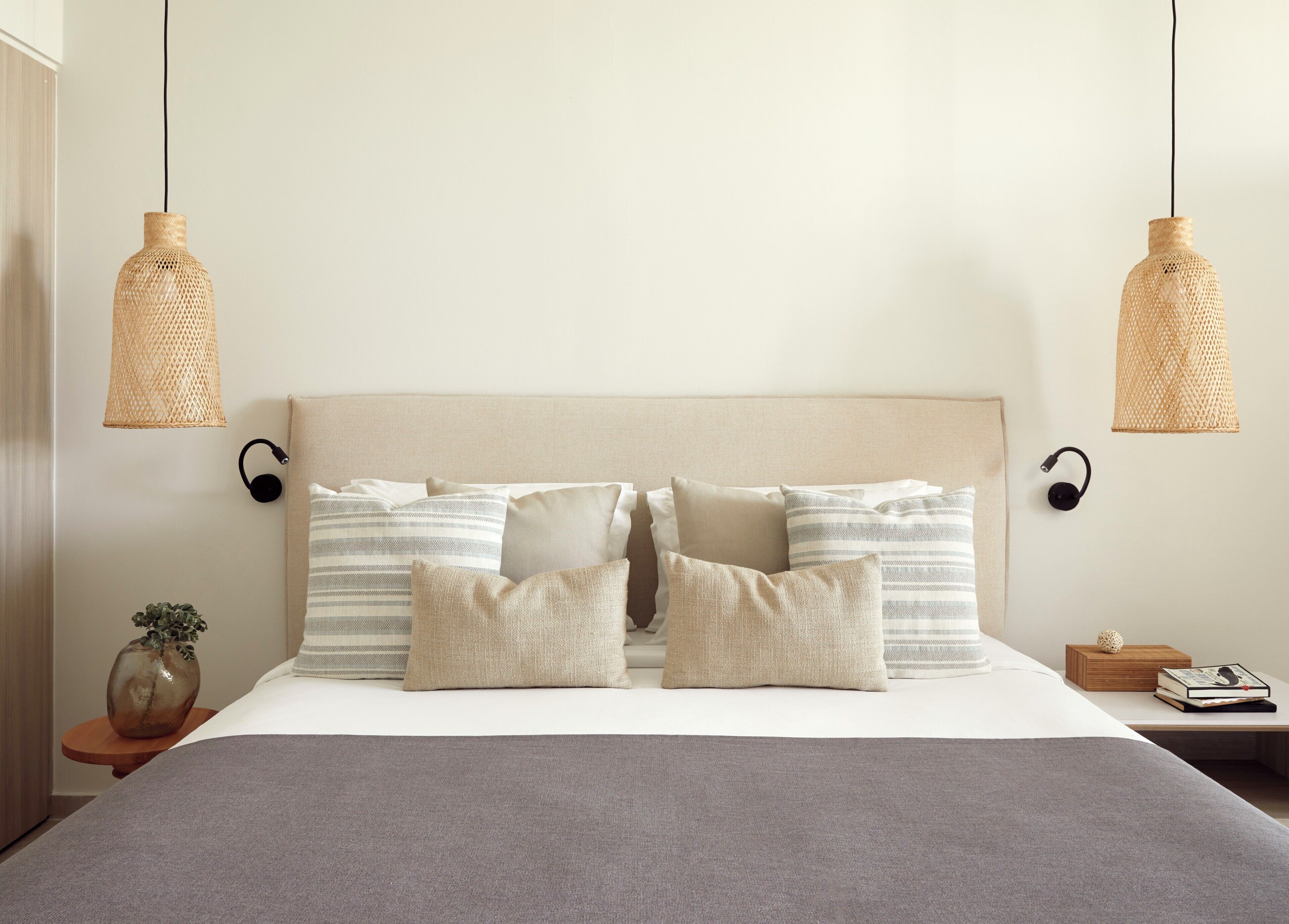 A neatly made bed with a grey blanket, multiple pillows, and two wall-mounted lamps.