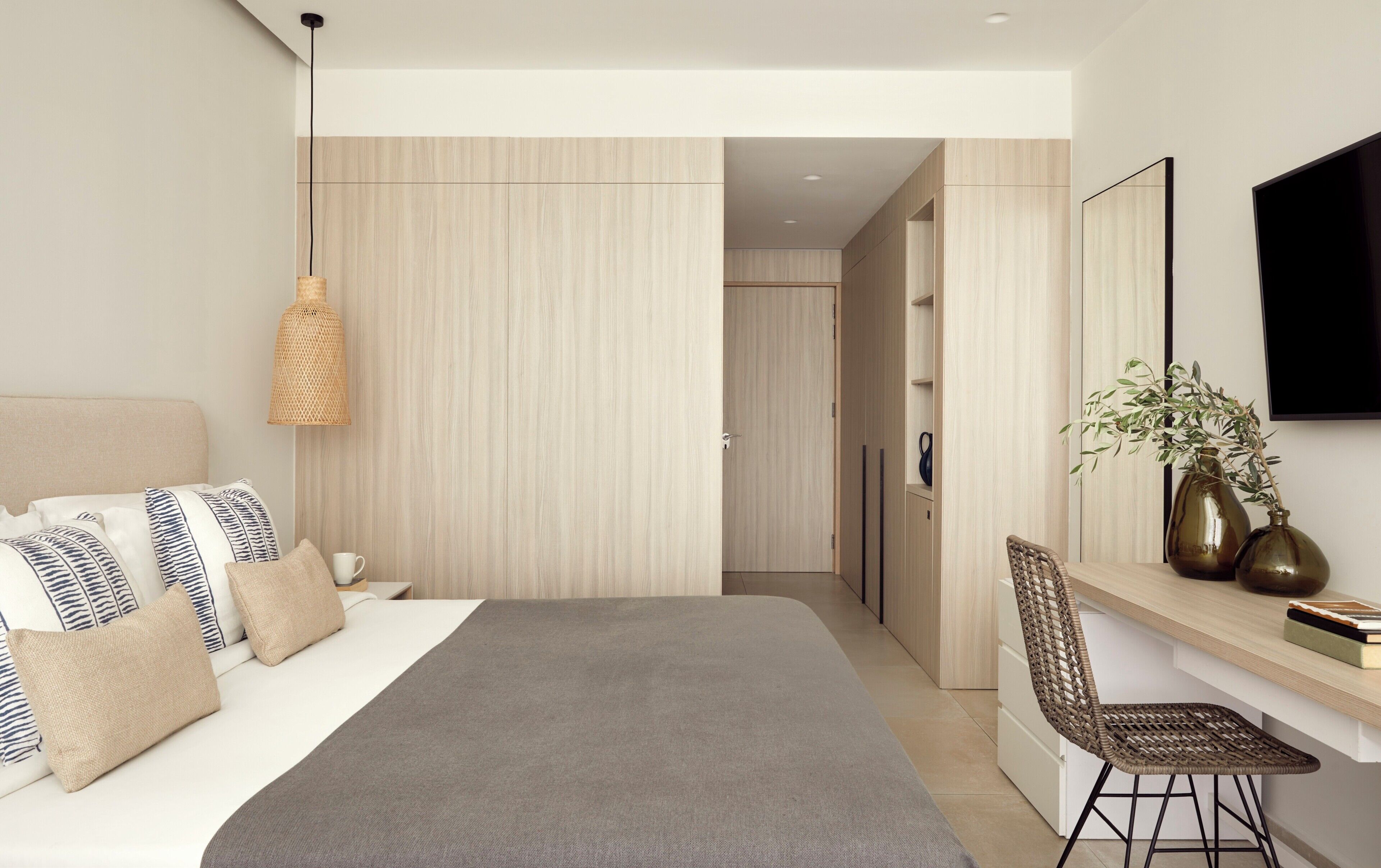 Een moderne slaapkamer met een bed, nachtkastje, lamp en uitzicht op een badkamer.