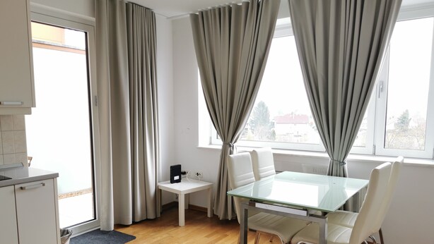 A modern room with a dining table, chairs, a small white table, and a kitchen area with a stove. - Trnovo Apartment (Ljubljana)