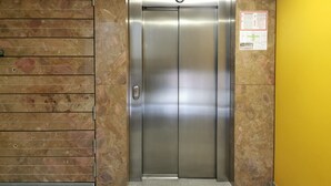 A metallic elevator door with a number "3" above it, a clock, and a safety sign on the wall. - Trnovo Apartment (Ljubljana)