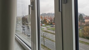 A view through a window with a handle, looking out at a cityscape with buildings, roads, and a distant hill. - Trnovo Apartment (Ljubljana)