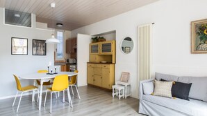 Une cuisine moderne avec des meubles blancs, une table à manger avec des chaises jaunes et un canapé gris.