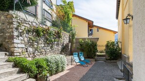 Une ruelle étroite avec des marches en pierre menant à un bâtiment jaune, un petit espace jardin avec un banc et une porte en métal.