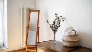 Une commode en bois avec un miroir, un vase décoré de verdure et un panier en osier contenant des serviettes.