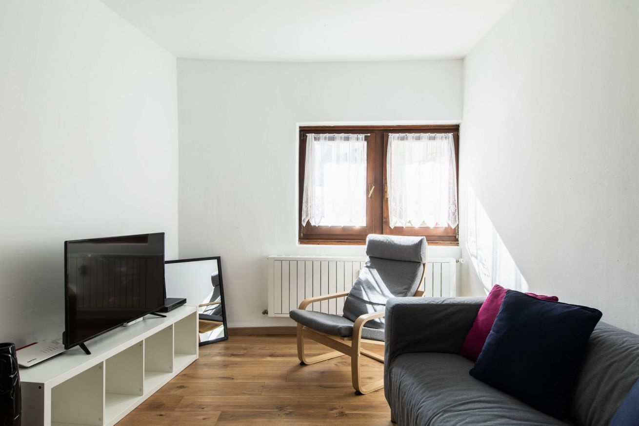 Ein Wohnzimmer mit Fernseher, einem Sessel, einer Couch und einem Fenster mit Vorhängen.