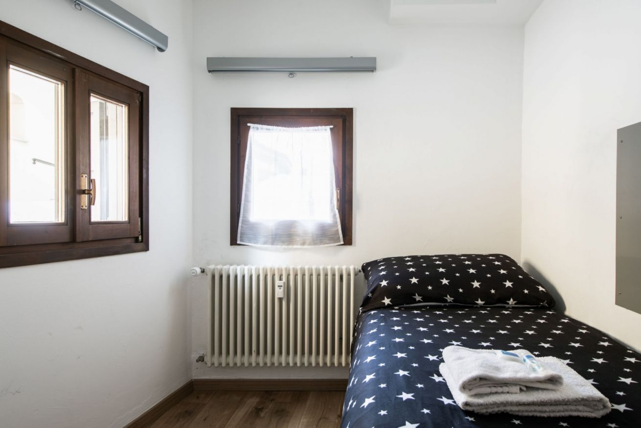 Ein Schlafzimmer mit einem Bett, einem Fenster mit Vorhängen, einem Heizkörper und einer Tür.