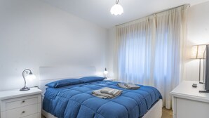 A bedroom with a bed, bedside tables, a lamp, and a window with curtains. - Modern APT in Tarvisio - 2 steps from the cycle route (Tarvisio)