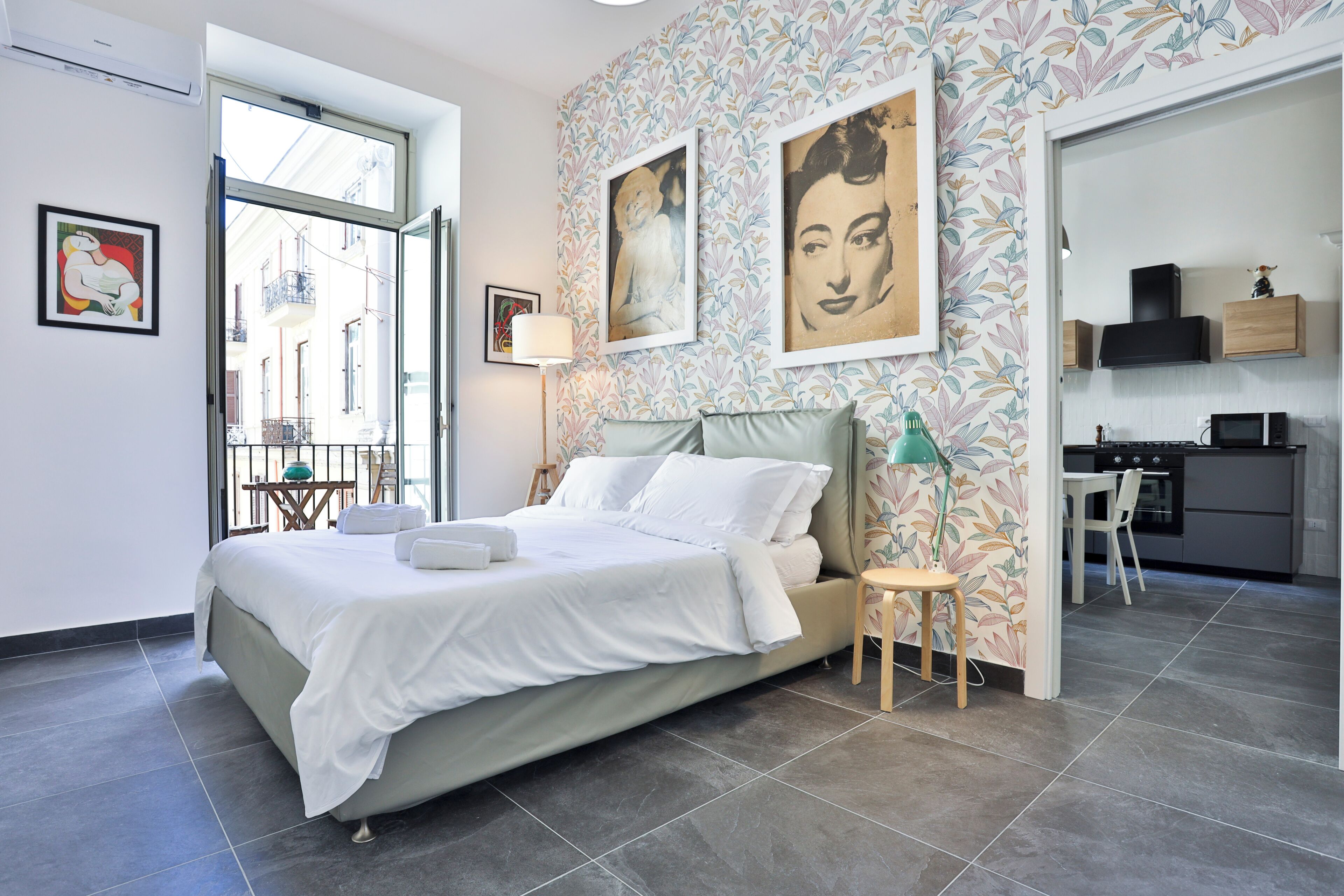 A modern bedroom with a large bed, a small table, a lamp, and a view of the outside.