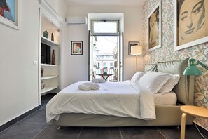 A bedroom with a bed, a bedside table, a lamp, a window, and a view of the street. - La finestra su Garibaldi (Naples)