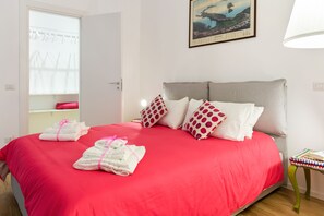 Ein ordentlich gemachtes Bett mit roter Bettwäsche, Kissen mit Punkten und gefalteten Handtüchern.