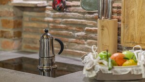 A kitchen counter with a stainless steel coffee pot, a wooden knife block, and a basket of fresh fruits. - Gorizia Sweet Minihouse with Parking (Gorizia)