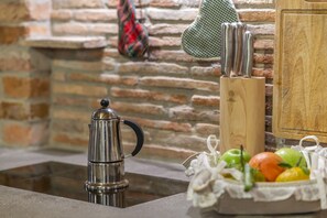 A kitchen counter with a stainless steel coffee pot, a wooden knife block, and a basket of fresh fruits. - Gorizia Sweet Minihouse with Parking (Gorizia)