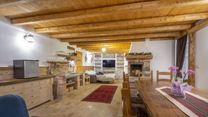 A cozy living room with a fireplace, wooden ceiling, and a dining area with a table and chairs. - Gorizia Sweet Minihouse with Parking (Gorizia)