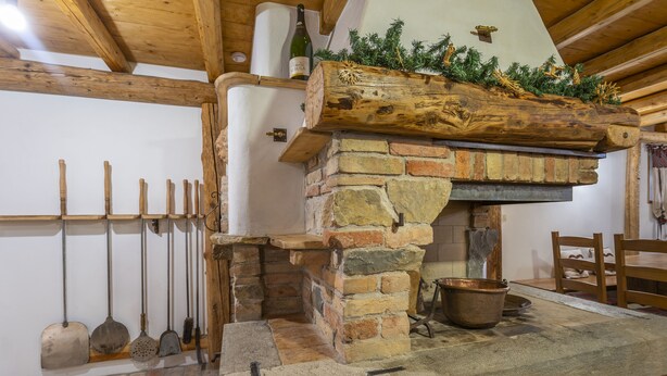 A rustic stone fireplace with a wooden mantel, surrounded by various tools and a rustic dining table. - Gorizia Sweet Minihouse with Parking (Gorizia)