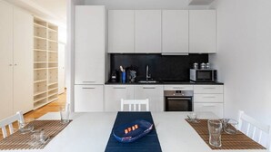 Une cuisine moderne avec des meubles blancs, un plan de travail noir et un coin repas avec une table dressée pour deux personnes.