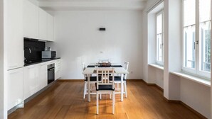 Une cuisine moderne avec des meubles blancs, un plan de travail noir et un coin repas comprenant une table et des chaises blanches.