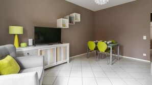 En moderne stue med et fladskærms-tv, et spisebord med stole og en sofa med puder.