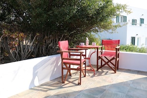 Una terraza con dos sillas rojas y una mesa, rodeada por un muro blanco y vegetación.