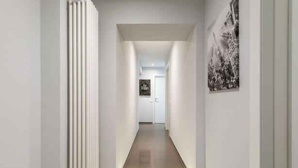 A modern hallway with a radiator, a door at the end, and a cityscape painting on the wall.