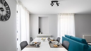A modern dining area with a white table set for two, a blue sofa, and a black wall clock.