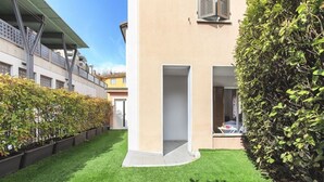 Ein modernes Gebäude mit Flachdach, einem kleinen Innenhof mit künstlichem Rasen und einer hohen Hecke.