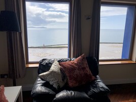 A room with a leather sofa facing a large window overlooking a beach.