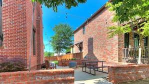 Ein Backsteinhaus mit Terrasse, Außenbereich mit Sitzgelegenheiten und einem Schild mit der Aufschrift 'Chelsea Cottage'.