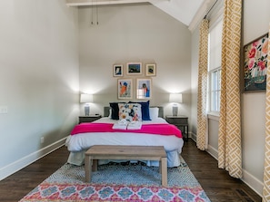 A bedroom with a bed, two bedside tables, a bench, a colorful rug, and framed artwork on the wall.