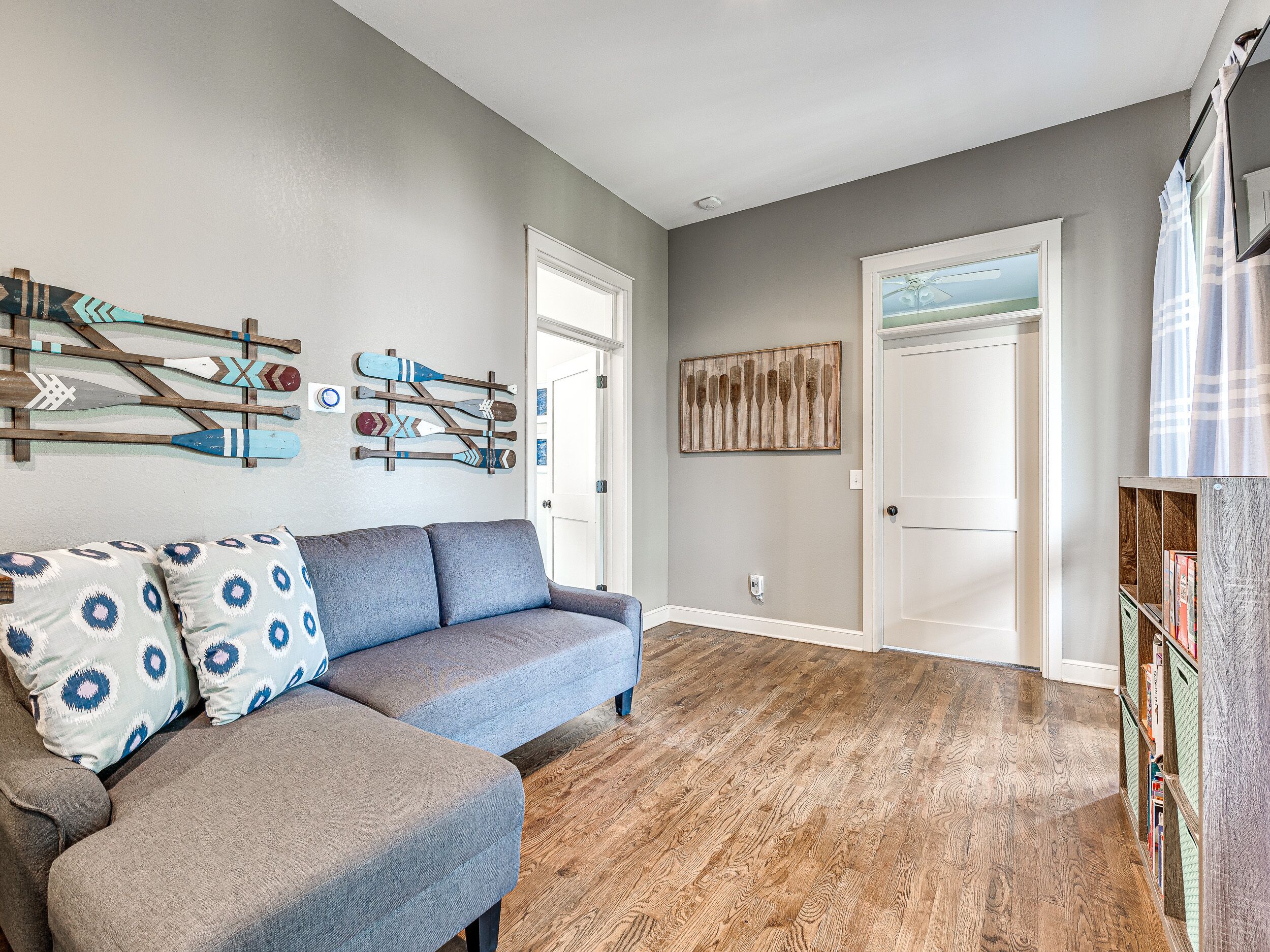 Een woonkamer met een grijze bank, houten vloeren en wanddecoratie, waaronder paddleboards en een houten paneel.