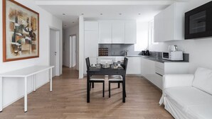 A modern kitchen with white cabinets, a dining table with chairs, and a white sofa. - Bright one-bedroom apartment 5 minutes from the center - MONTARINA (Lugano)