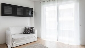A minimalist living room with a white sofa, a grey rug, and a large window with sheer curtains. - Bright one-bedroom apartment 5 minutes from the center - MONTARINA (Lugano)
