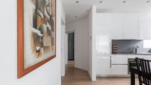 A modern kitchen with white cabinets, a black countertop, and a dining area with a black chair. - Bright one-bedroom apartment 5 minutes from the center - MONTARINA (Lugano)
