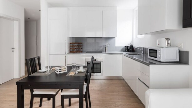 A modern kitchen with white cabinets, a black dining table, and a microwave. - Bright one-bedroom apartment 5 minutes from the center - MONTARINA (Lugano)