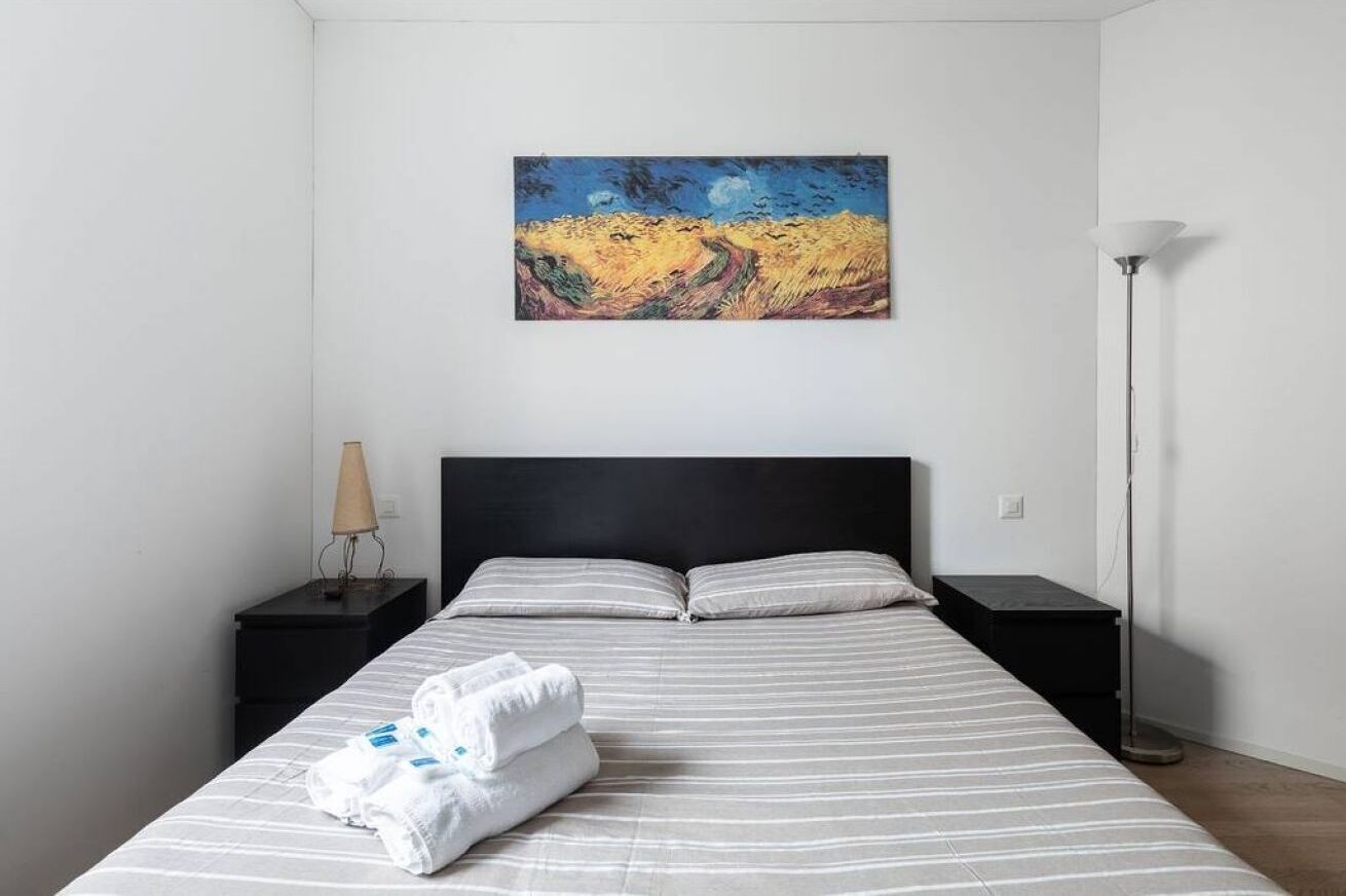 A hotel room with a bed, two bedside tables, a lamp, and a painting on the wall.