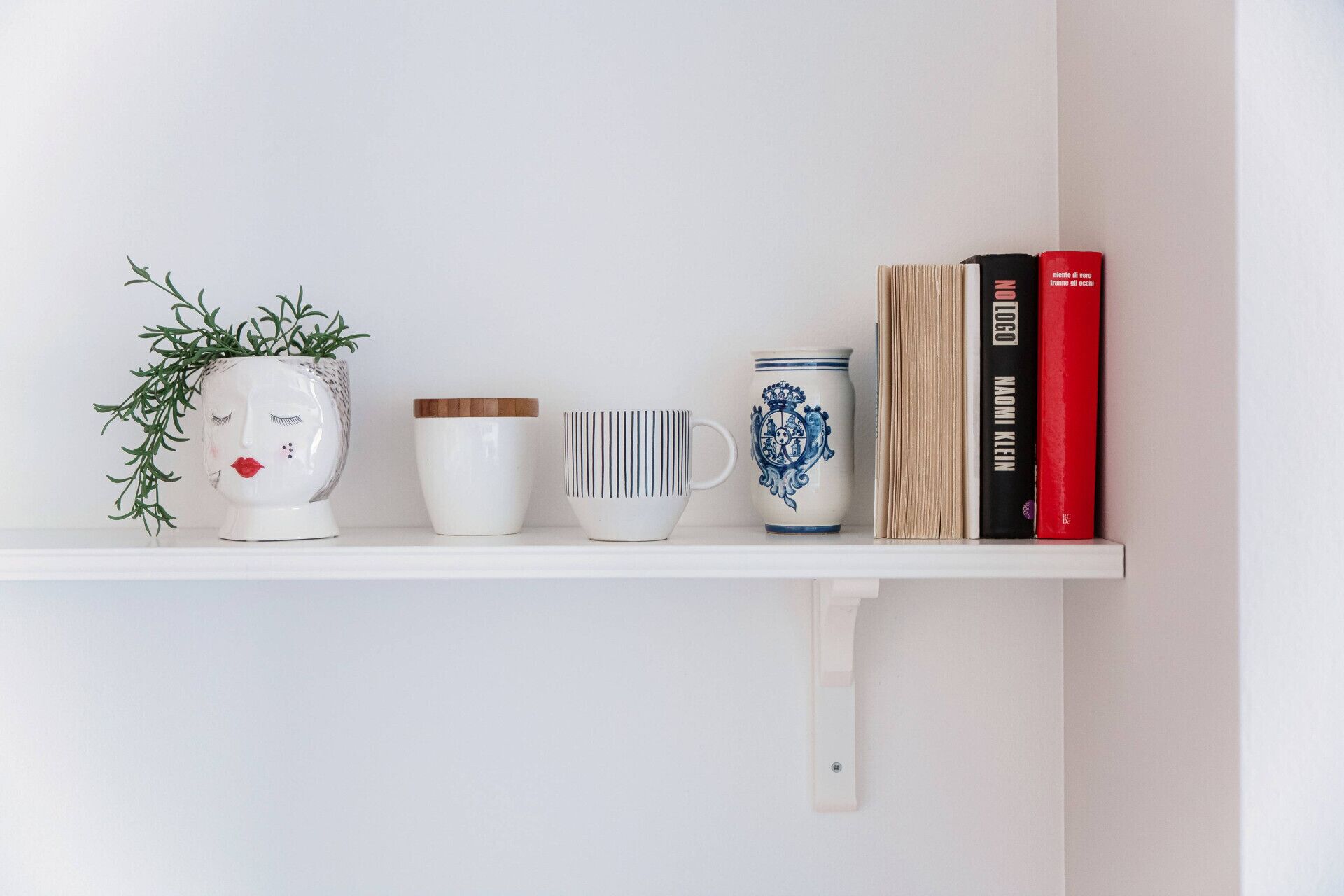 Une étagère avec une plante en pot, une tasse blanche, une tasse en céramique bleue et blanche, et deux livres.
