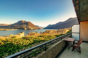 Un balcón con mesa y sillas que da a un lago y montañas.