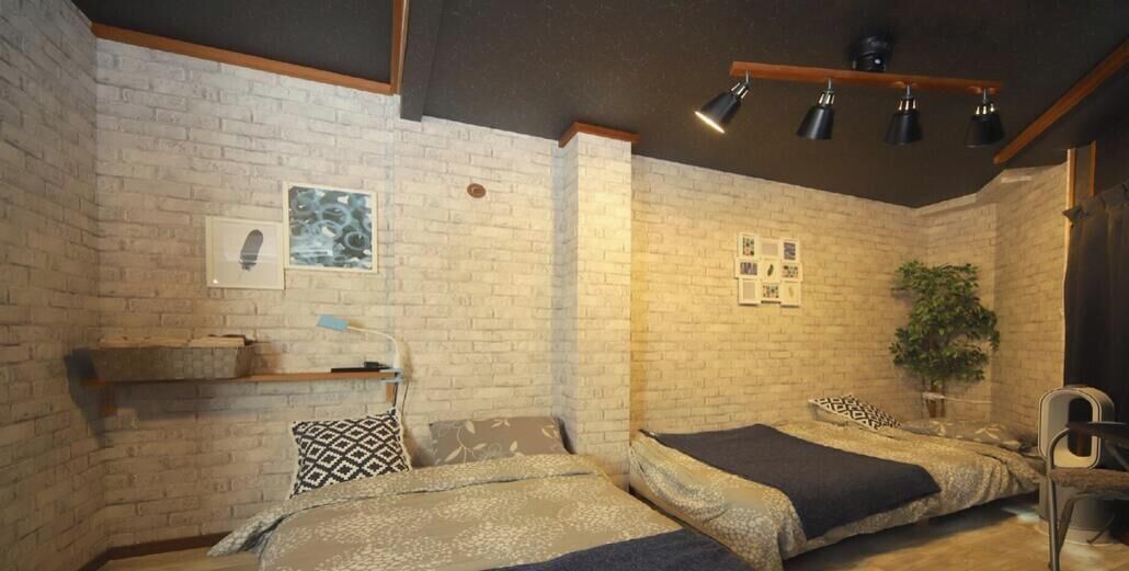 Ein Zimmer mit zwei Betten, einer Ziegelwand, einem Regal mit einer Pflanze und einer Deckenleuchte.
