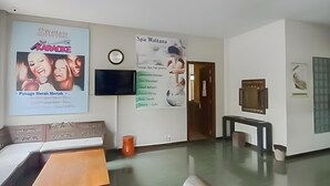 Vestíbulo de hotel con un cartel grande que anuncia un evento de karaoke, servicios de spa y un reloj en la pared.