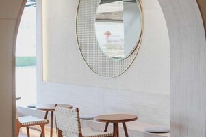 Um interior moderno com um espelho redondo, cadeiras de madeira e pequenas mesas redondas.