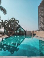 Piscina com água cristalina, cercada por palmeiras e um edifício moderno com estrutura em formato de coração.
