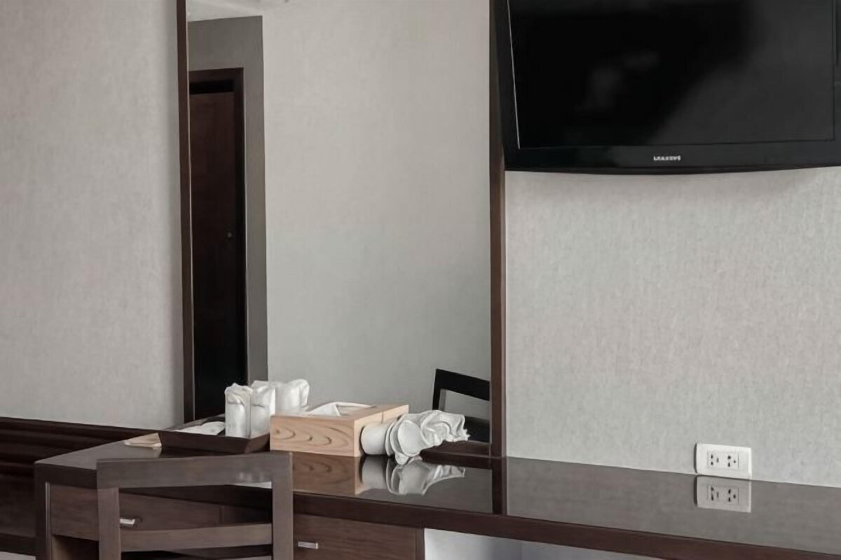 Ett hotellrum med ett skrivbord i trä, en stol, en platt-TV som är monterad på väggen och en spegel.