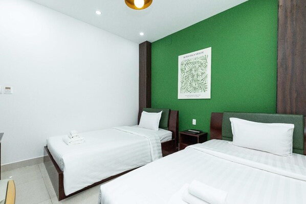 A hotel room with two beds, a green accent wall, a framed botanical print, and a wooden headboard.