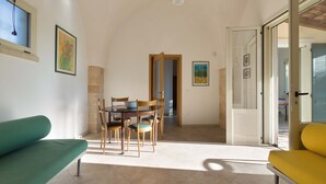 Un espace repas comprenant une table et des chaises, un canapé et une porte-fenêtre coulissante donnant sur un espace extérieur.