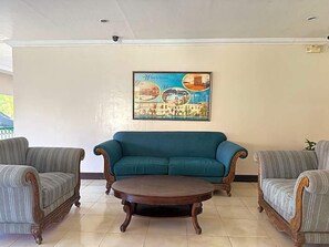 A room with a teal sofa, two striped armchairs, and a round wooden coffee table. A framed picture of a coastal scene is on the wall. - Dotties Place Hotel and Restaurant (Butuan)