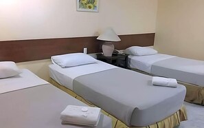 A hotel room with two beds, a nightstand with a lamp, and a small table with a folded towel. - Dotties Place Hotel and Restaurant (Butuan)