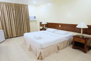A hotel room with a bed, two bedside tables, a lamp on each table, a curtain, and an air conditioning unit. - Dotties Place Hotel and Restaurant (Butuan)