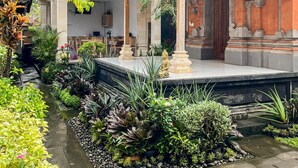 A traditional building with a tiled roof, a covered patio area, and a small water feature with plants. - Dono Guest House (Ubud)