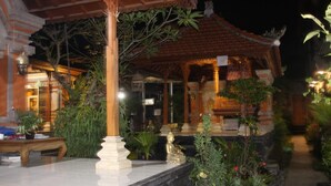 An outdoor area with a covered seating area, plants, and a statue. - Dono Guest House (Ubud)