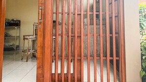 A wooden gate with vertical bars, leading to a room with a tiled floor and a chair. - Dono Guest House (Ubud)