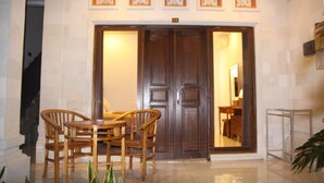 A hotel lobby with a large wooden door, a dining table with chairs, and a small plant. - Dono Guest House (Ubud)